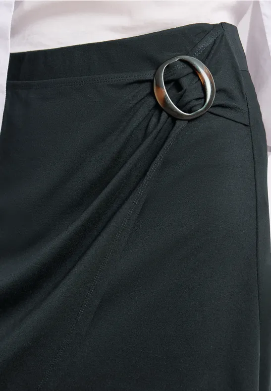 Nahaufnahme eines schwarzen Wickelrocks mit rundem Metall-Detail am Bund.