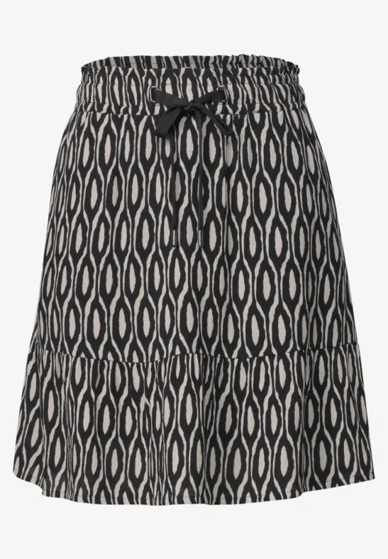Jupe courte noire à motifs blancs organiques, taille élastique et petit nœud décoratif à l’avant.