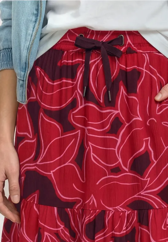 Wijde rode broek met bloemmotief en tailleband, gecombineerd met een wit shirt en een spijkerjasje.