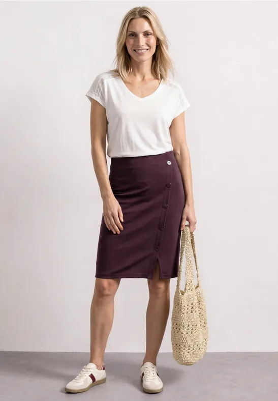 Vrouw met wit T-shirt, bordeaux midi-rok met knopen, witte sneakers en een netzak