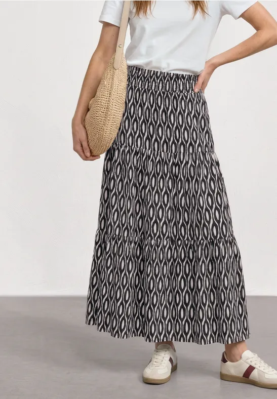 Een vrouw draagt een wit T-shirt, een zwart-witte maxi-rok met geometrisch patroon en witte sneakers.