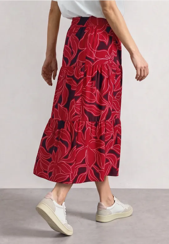 Vrouw in een rode, bloemenprint midi-rok met volant en witte sneakers.