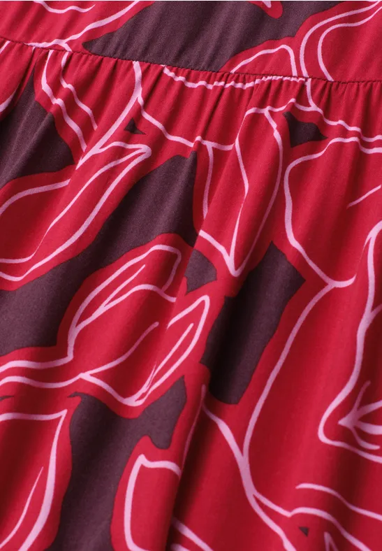 Close-up van rood stof met witte, abstracte bloemenprint en geplooide naad.