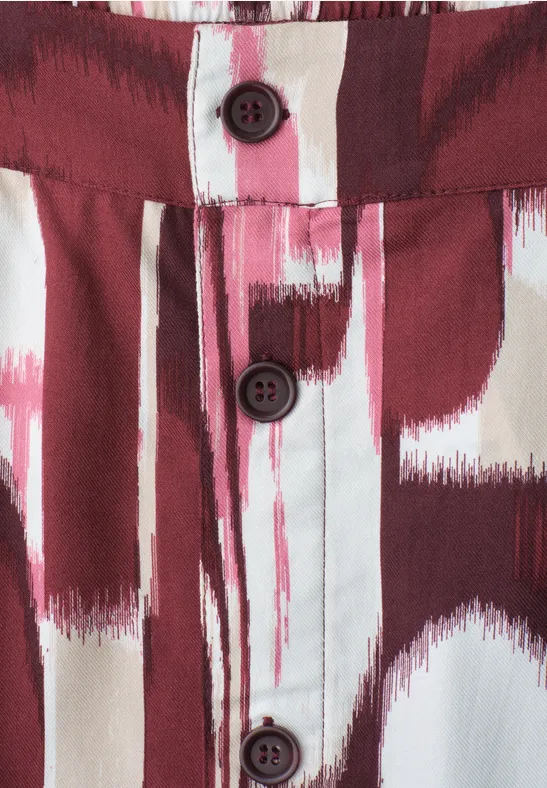 Detail van een overhemd met rood-witte schilderachtige penseelstreekprint en drie donkere knopen.