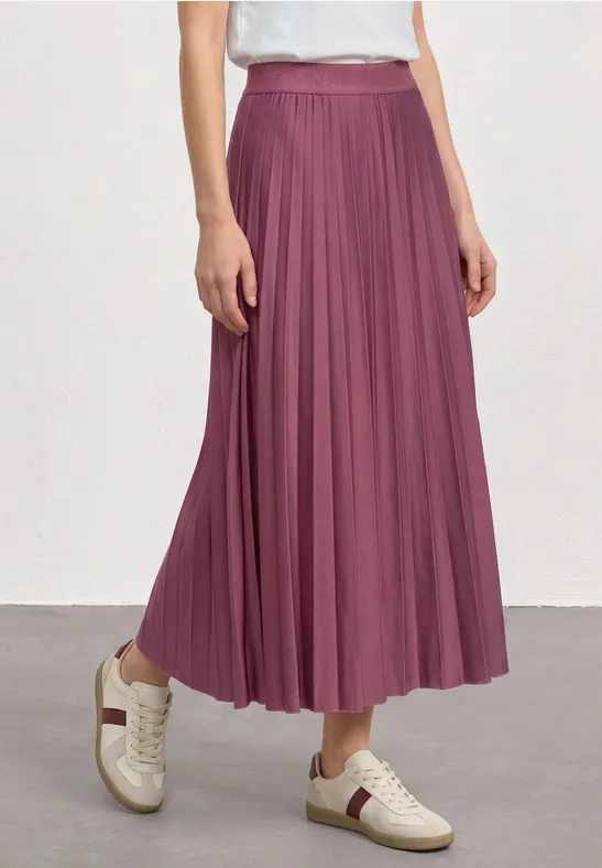 Een persoon draagt een lange geplooide pruimkleurige rok met witte sneakers.