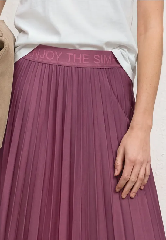Een pruimkleurige, geplooide midirok met elastische tailleband 'ENJOY THE SIMPL...' en wit shirt.