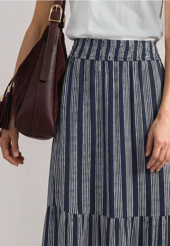 Frau trägt weiße Bluse und blau-weiß gestreiften Maxi-Rock, dazu eine braune Schultertasche.
