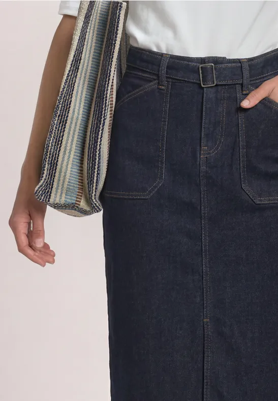 Vrouw draagt een donkere denim midirok met opgestikte zakken en riem, gecombineerd met wit T-shirt en gestreepte tas.