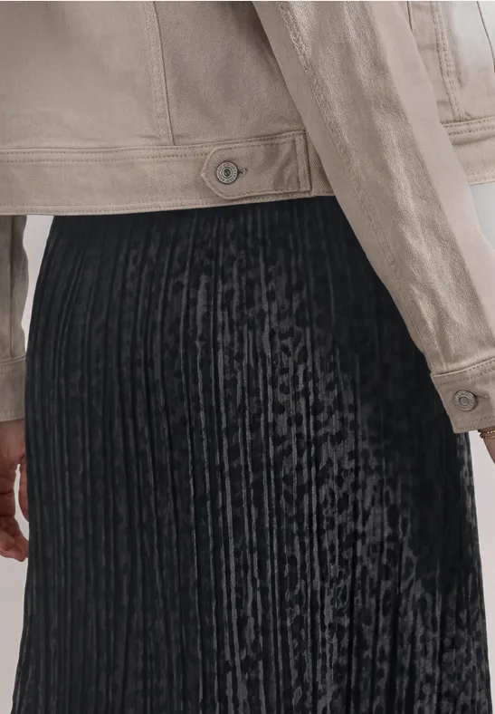 Close-up van een persoon met zilveren jas en zwarte, geplooide fluwelen rok.
