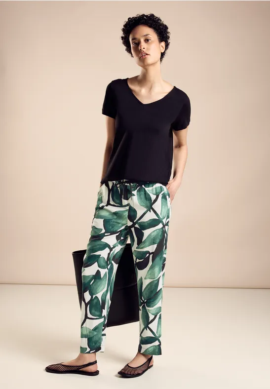 Frau mit schwarzem Shirt und grüner gemusterter Hose, entspannte Pose.
