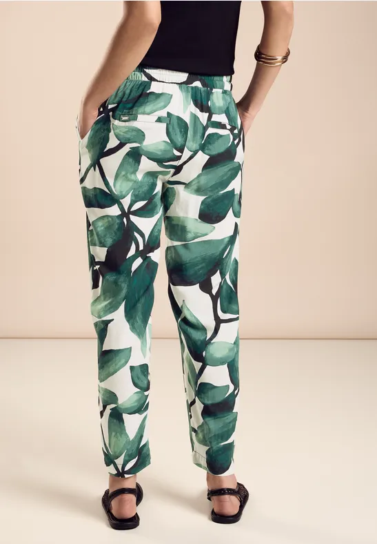 Hose mit grünem Blätterprint, schwarze Sandalen, schwarze Oberteil.