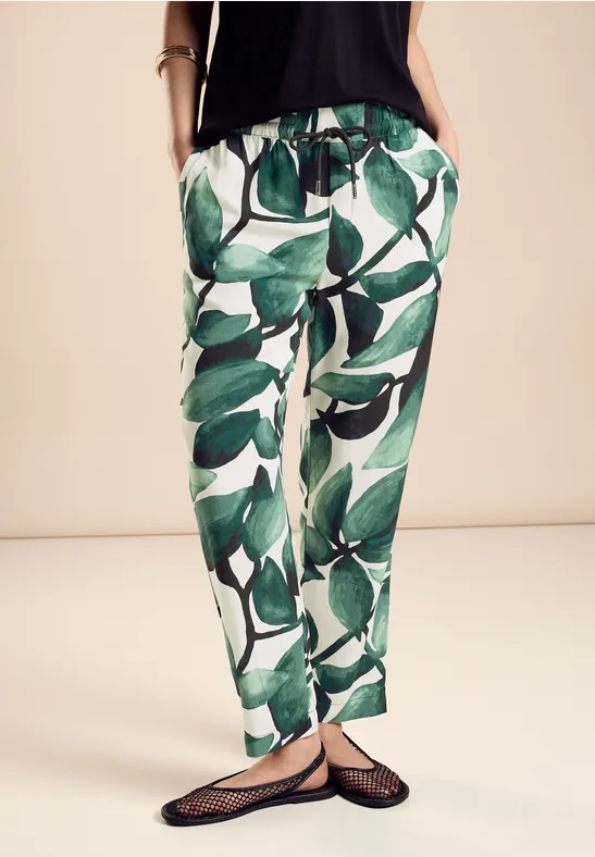 Weiße Hose mit grünem Blattmuster, schwarze Oberteil und Sandalen.