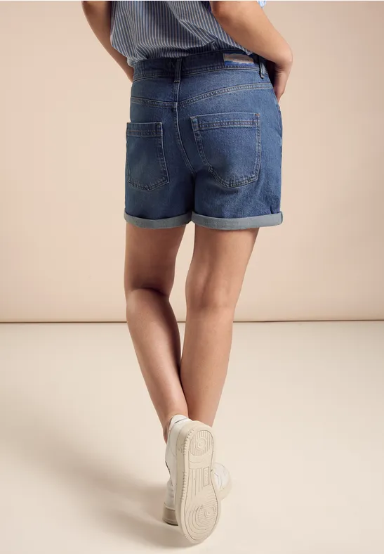 Person in Jeansshorts und weißen Sneakern, von hinten fotografiert.