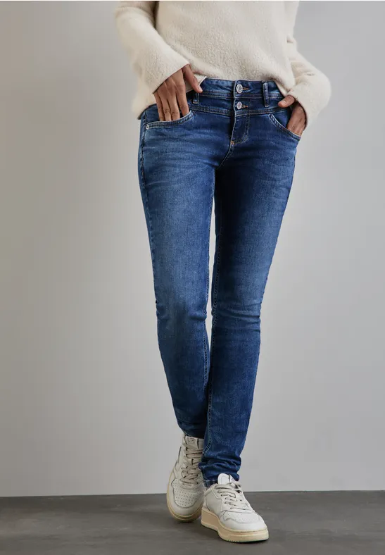 Person trägt blaue Jeans, weißen Pullover und weiße Sneaker.