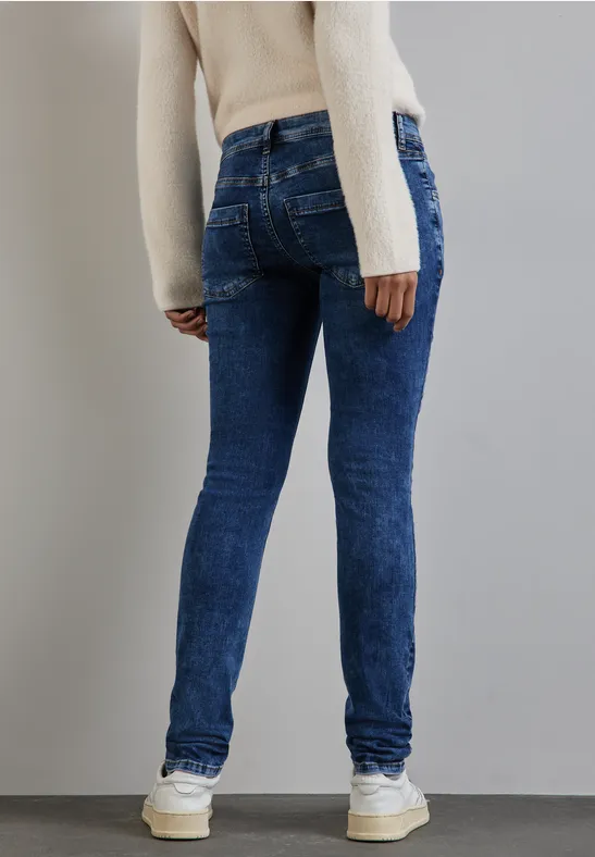 Person in blauer Jeans und weißem Pullover steht mit dem Rücken zur Kamera.