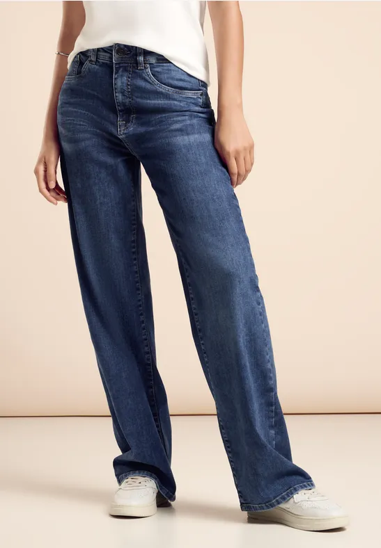 Frau trägt eine weite Blue Jeans und weiße Sneaker.