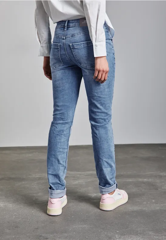 Person mit Jeans und weißen Sneakern steht auf grauem Boden, von hinten gesehen.