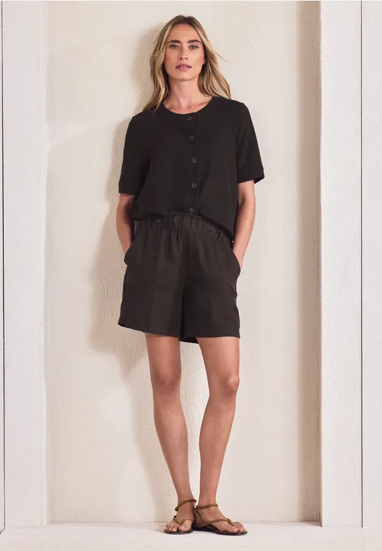 Vrouw in zwart T-shirt en korte broek met sandalen staat in een lichte, strakke nis.