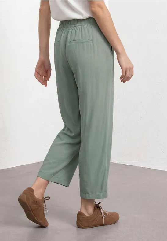 Een persoon draagt losse, groengrijze broek tot de enkels met elastische taille en bruine veterschoenen.