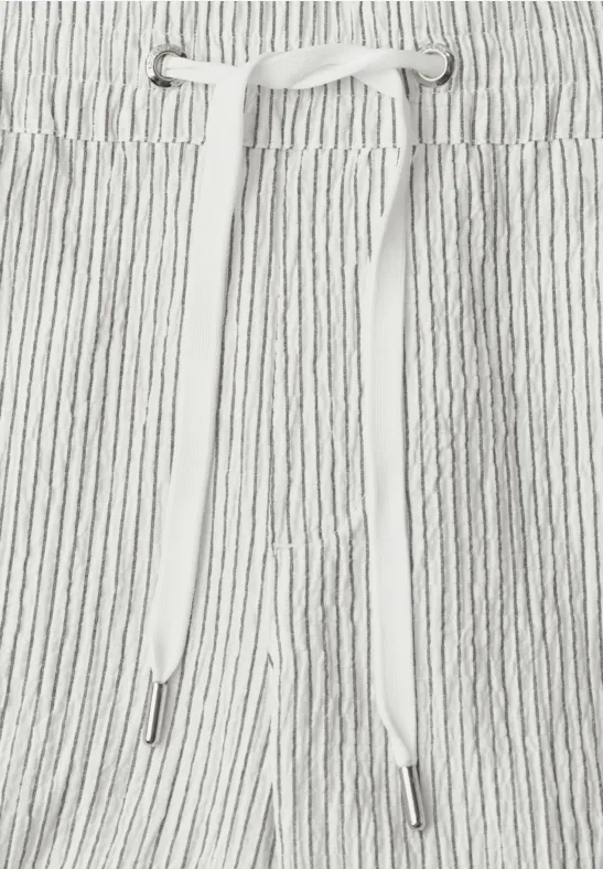 Close-up van een wit-grijs gestreepte stoffen tailleband met tunnelkoord en witte bindlinten.