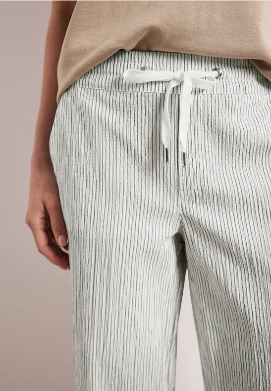 Close-up van een persoon in licht gestreepte, losvallende stoffen broek met trekkoord en beige bovenstuk.