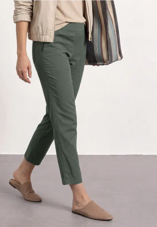 Persoon met olijfgroene broek, beige schoenen en een gestreepte tas.