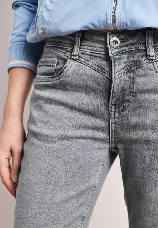 Eine Person in hellblauer Jacke und grauen Jeans, Nahaufnahme des Rumpfes mit sichtbarer Hand.