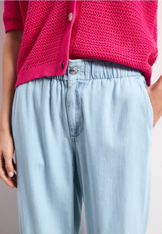 Een persoon draagt een roze gebreid vest en een lichtblauwe wijde broek.