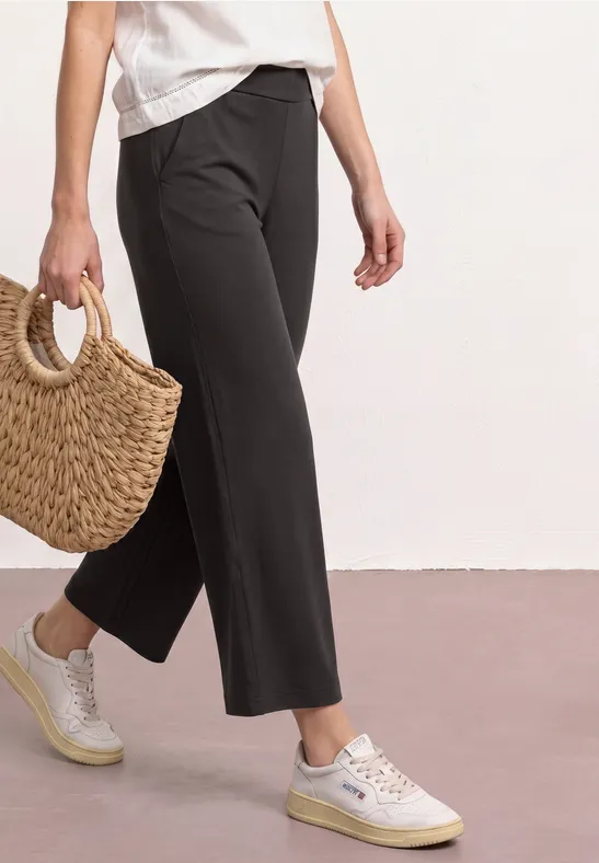 Zwarte 7/8-broek, witte sneakers en gevlochten strozak op lichte ondergrond