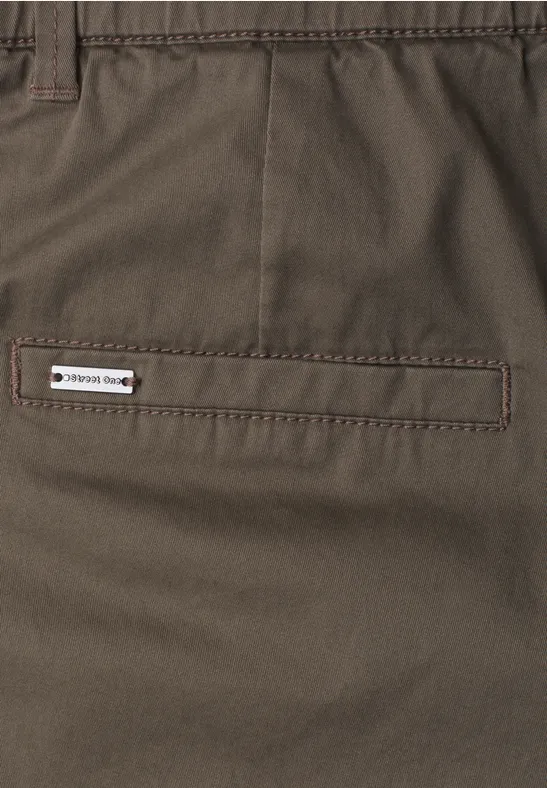 Bruine broek met achterzakdetail en klein wit label 'TREKKING SHOP'.
