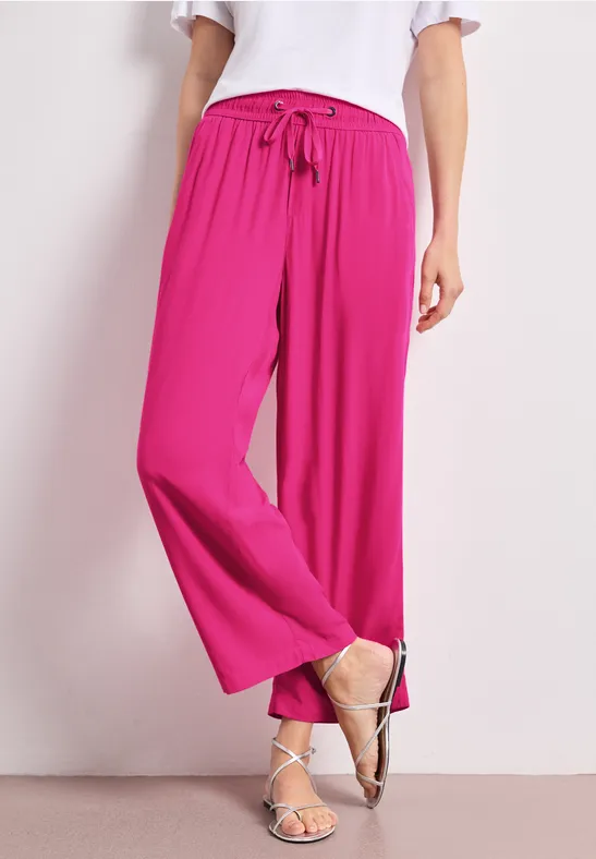 Femme porte un pantalon palazzo rose à cordon avec un haut blanc devant un fond clair.