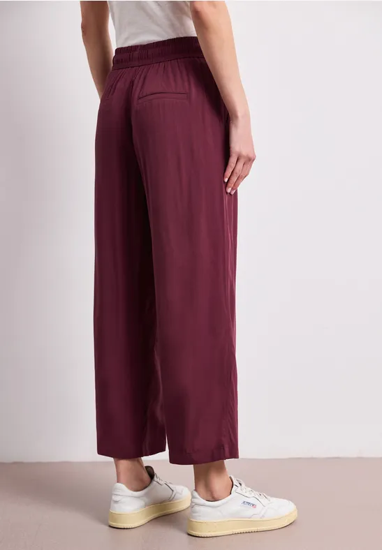 Achteraanzicht van een bordeauxrode, wijdvallende broek met elastische taille en witte sneakers.