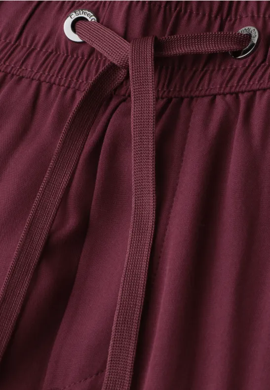 Close-up van een bordeauxrode broek met trekkoord en elastische taille.
