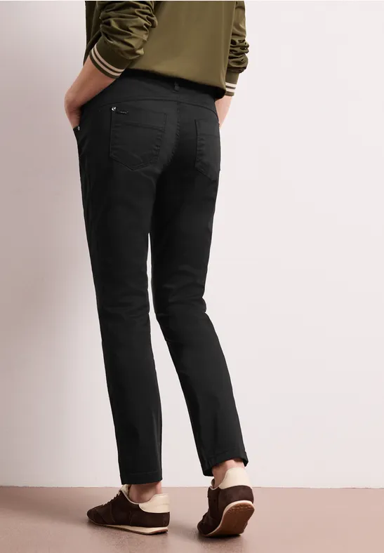 Vue arrière d’une personne portant un pantalon noir droit et des mocassins marron sur fond clair.