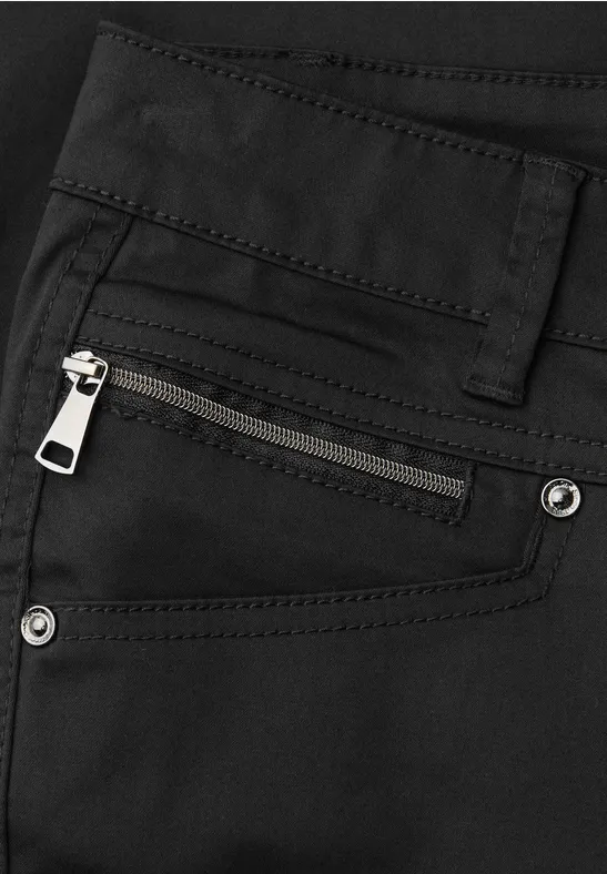 Gros plan d'un pantalon noir avec poche zippée apparente, passant de ceinture et rivets.