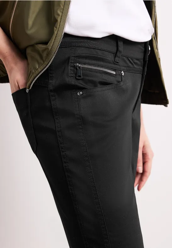Pantalon noir ajusté avec plusieurs poches zippées, porté avec un t-shirt blanc et un haut vert.