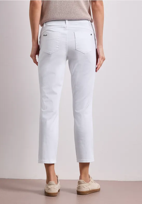 Rückansicht einer Person in weißen Jeans und beigen Schuhen vor neutralem Hintergrund.