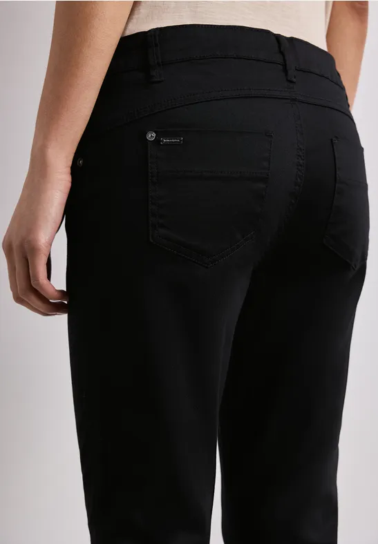 Rückansicht einer Person in schwarzen Jeans vor neutralem Hintergrund.
