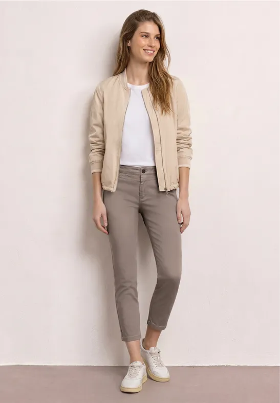 Jeune femme en look casual : blouson beige, t-shirt blanc, pantalon taupe et baskets blanches.