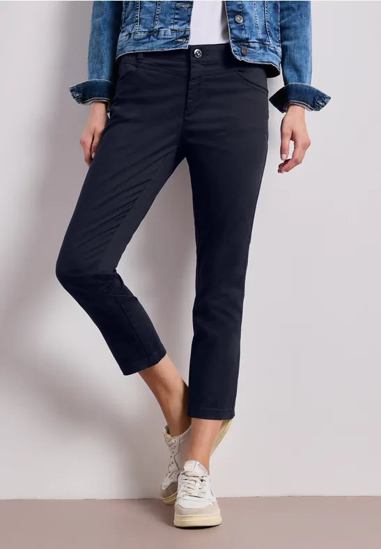 Een persoon draagt zwarte 7/8-broek, witte sneakers en een spijkerjack.
