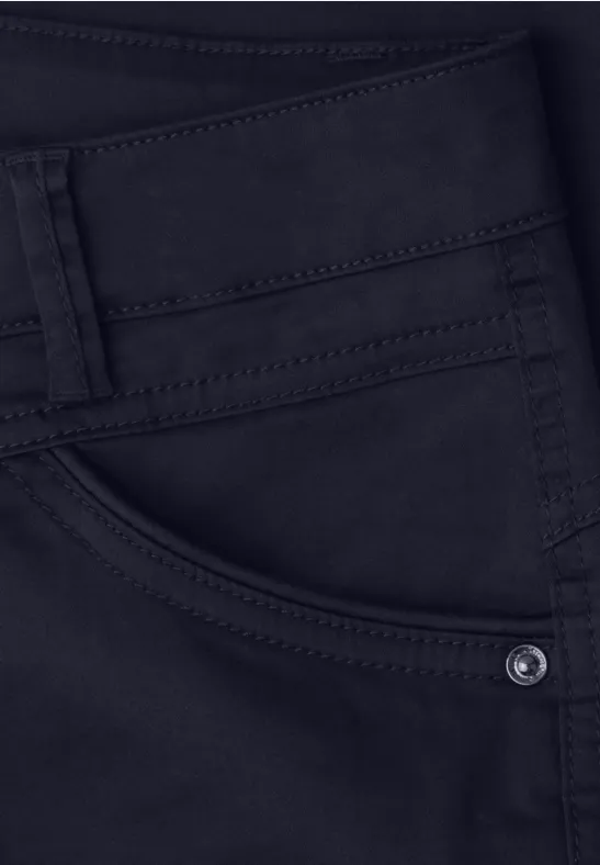 Donkere spijkerbroek in close-up met zichtbare voorzak, stiksels en riemlussen.