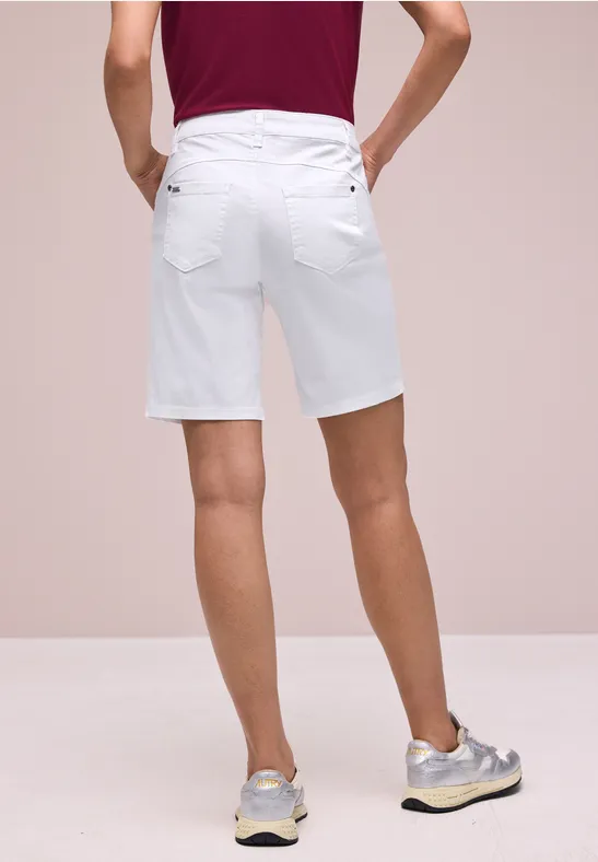 Een man van achteren in witte korte broek tot aan de knieën met grijze sneakers tegen een neutrale achtergrond.