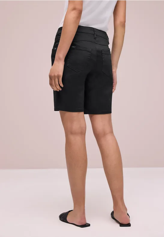 Vue arrière d’une personne portant un short bermuda noir, un t-shirt blanc et des sandales noires sur fond clair.