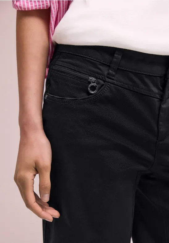 Gros plan sur une personne en jean noir et chemise rose rayée, main détendue sur la hanche.