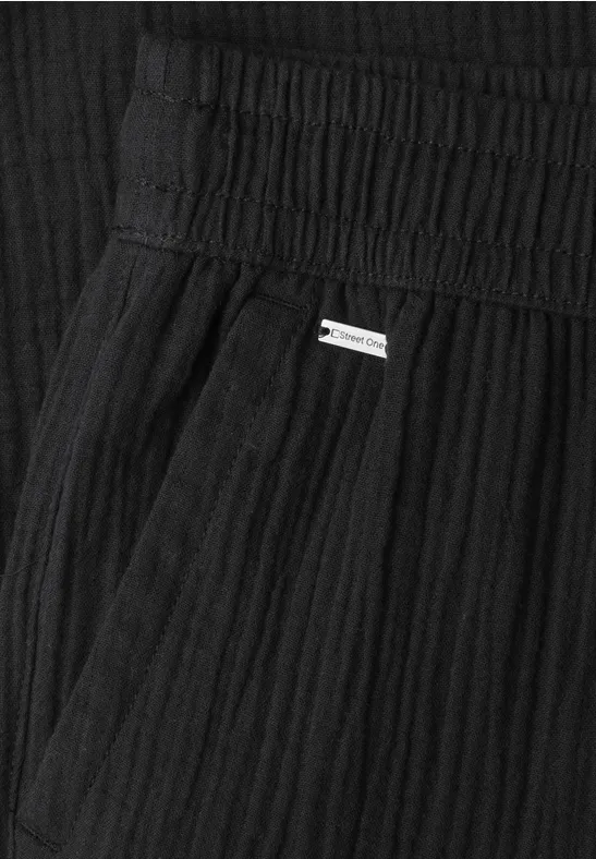 Close-up van een zwart geplooid kledingstuk met elastische tailleband en klein metalen label.