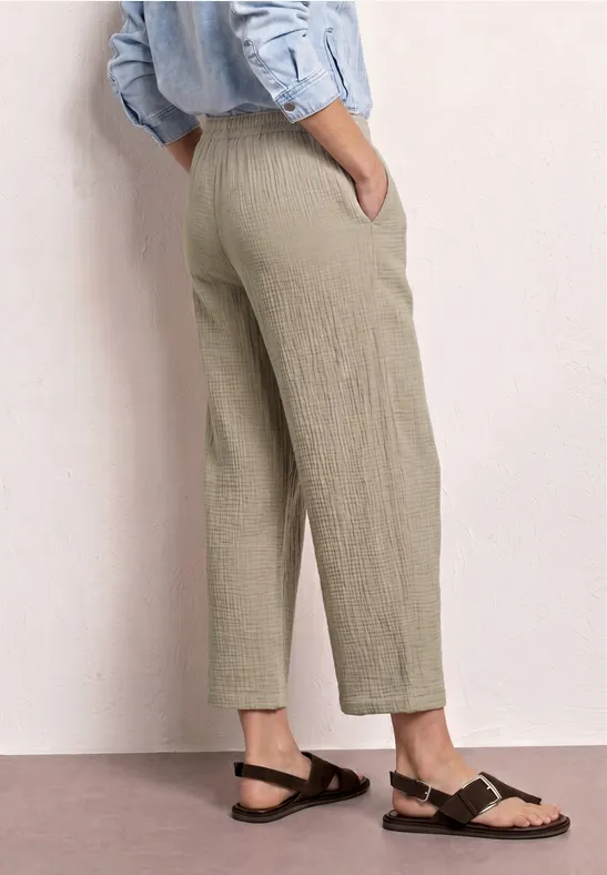 Achteraanzicht van een persoon in licht, loszittend linnen broek met zakken en zwarte sandalen.