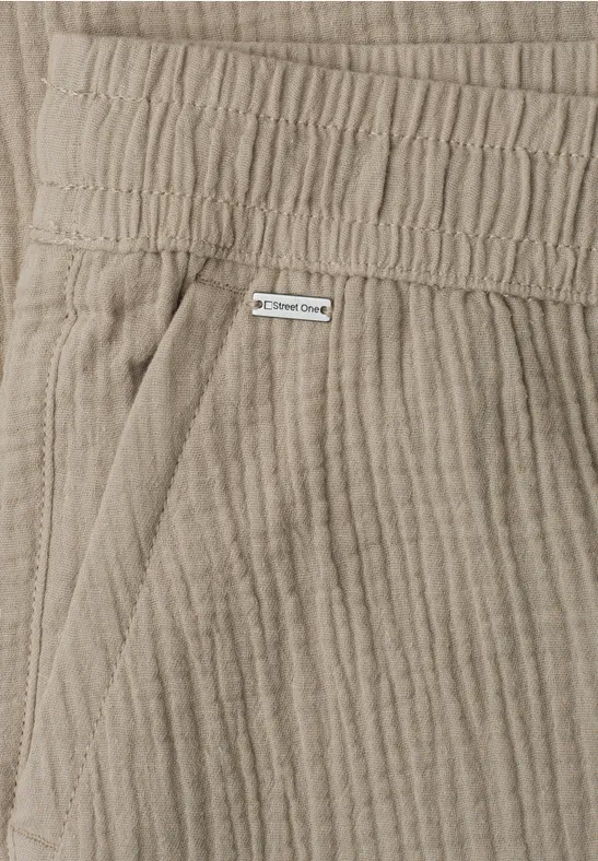 Close-up van een beige corduroy broek met elastische taille, zijzak en klein label