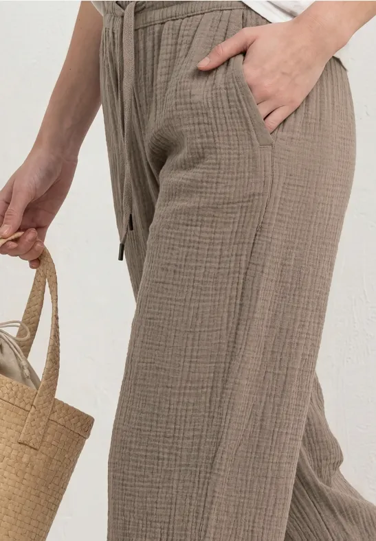 Vrouw in wijde beige katoenen broek met strikkoord en zakken, houdt een strooien mand vast