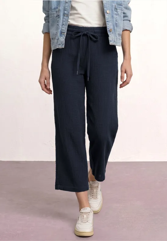 Vrouw met wijde marineblauwe broek met tunnelkoord, spijkerjasje en witte schoenen