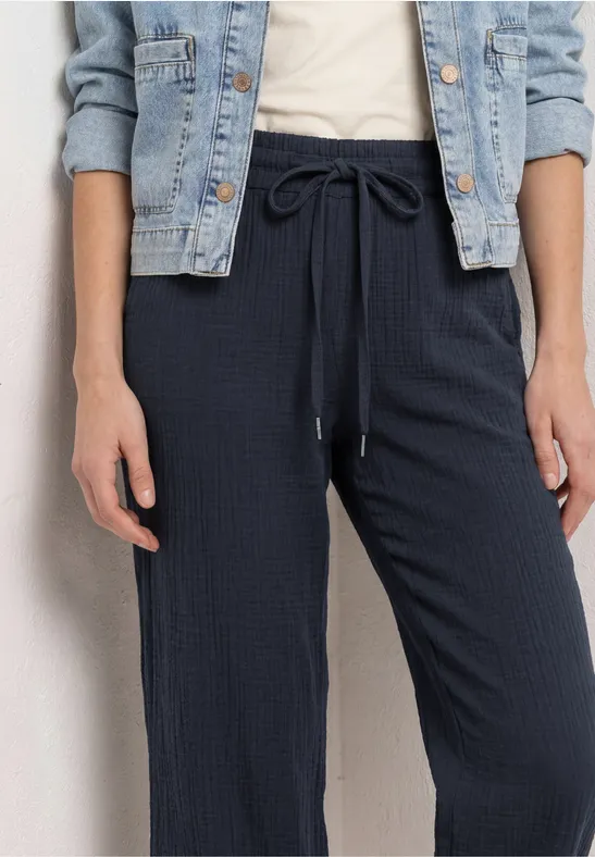 Persoon draagt donkerblauwe, wijde broek met trekkoord en een lichtblauwe spijkerjas.